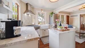 A modern kitchen with a coffee maker, stove, and white cabinetry. - 3999 Stay at "Cottage by the Sea" in Monterey (Monterey)