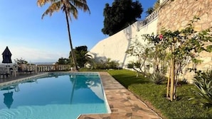 Une piscine dotée d’une terrasse carrelée en pierre, entourée de verdure et bordée d’un mur en pierre.