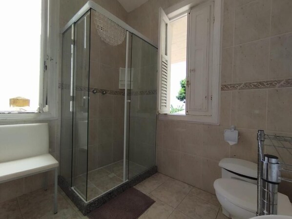 Een badkamer met een douchecabine van glas, een toilet en een bankje.