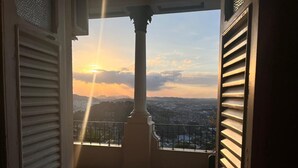 Un balcon ouvert offrant une vue sur le paysage urbain et les montagnes au coucher du soleil.