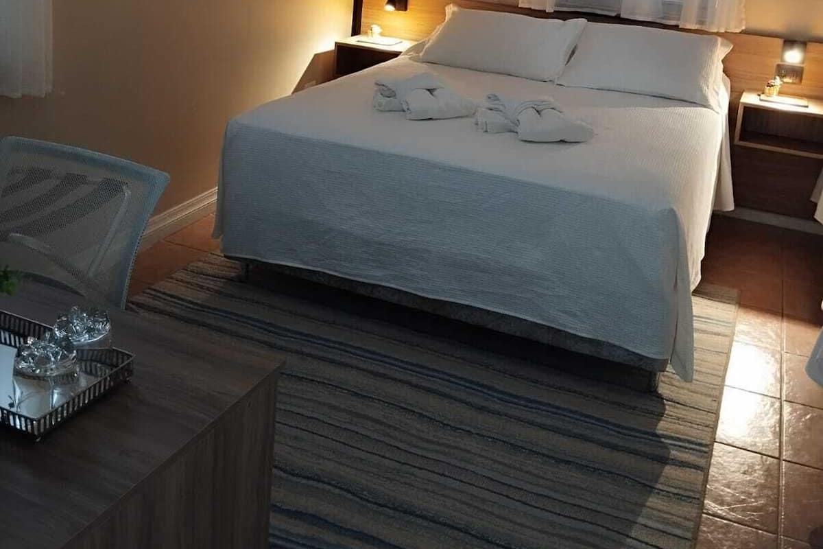 A hotel room with a bed, a bedside table, a lamp, a window with curtains, and an air conditioning unit.