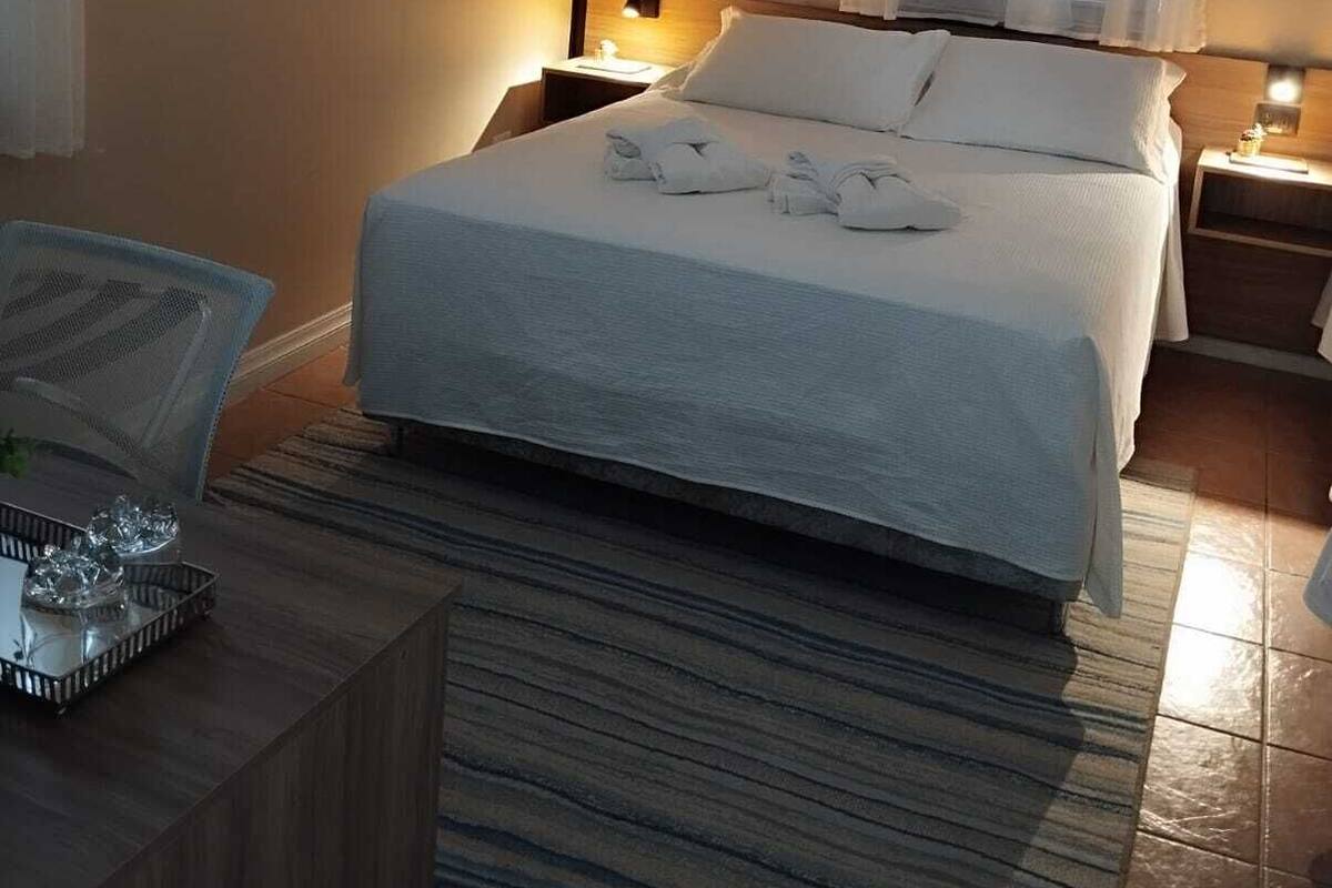 A hotel room with a bed, a bedside table, a lamp, a window with curtains, and an air conditioning unit.
