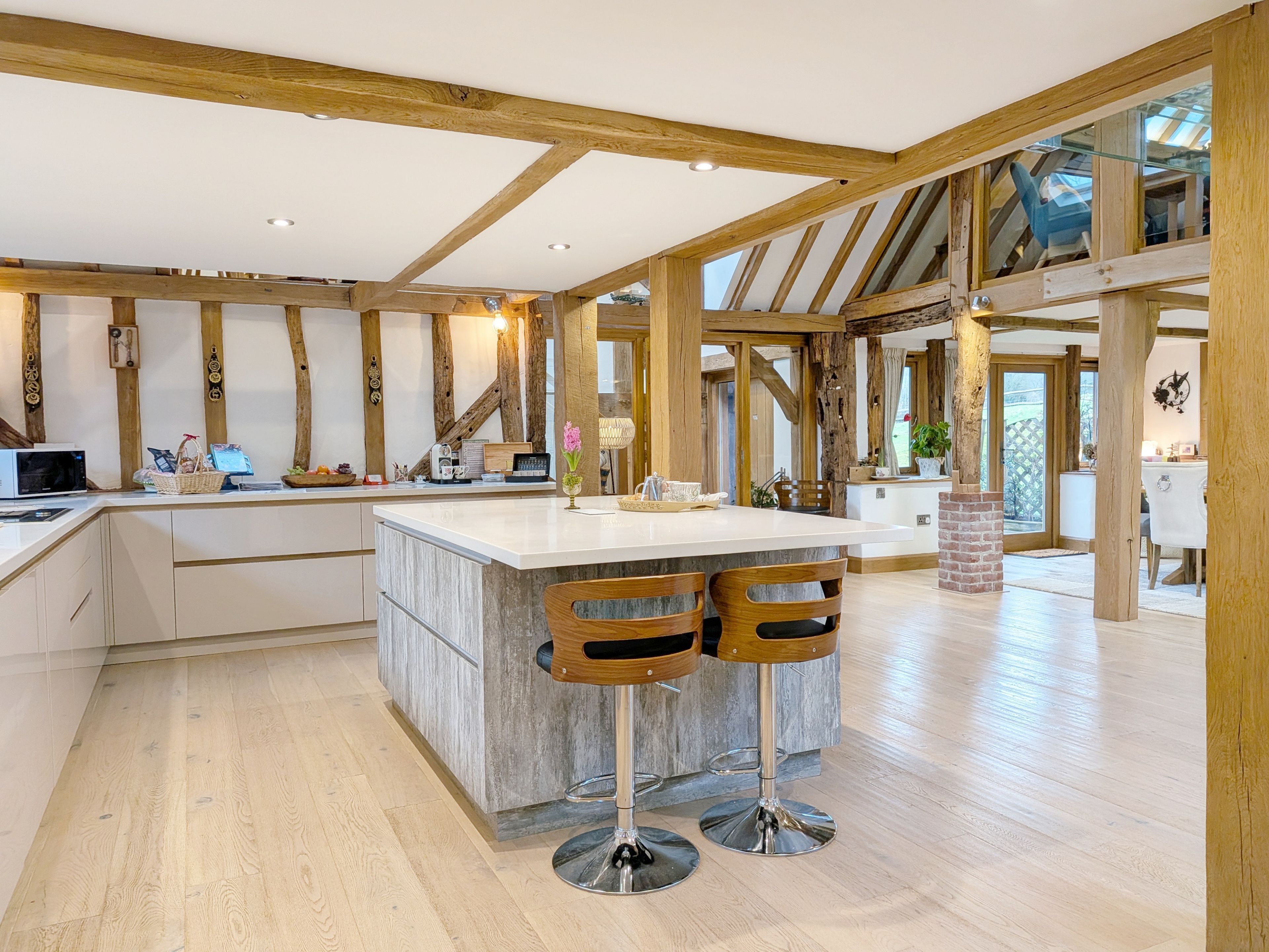 A spacious kitchen with a large island, wooden beams, and a view to the outside.