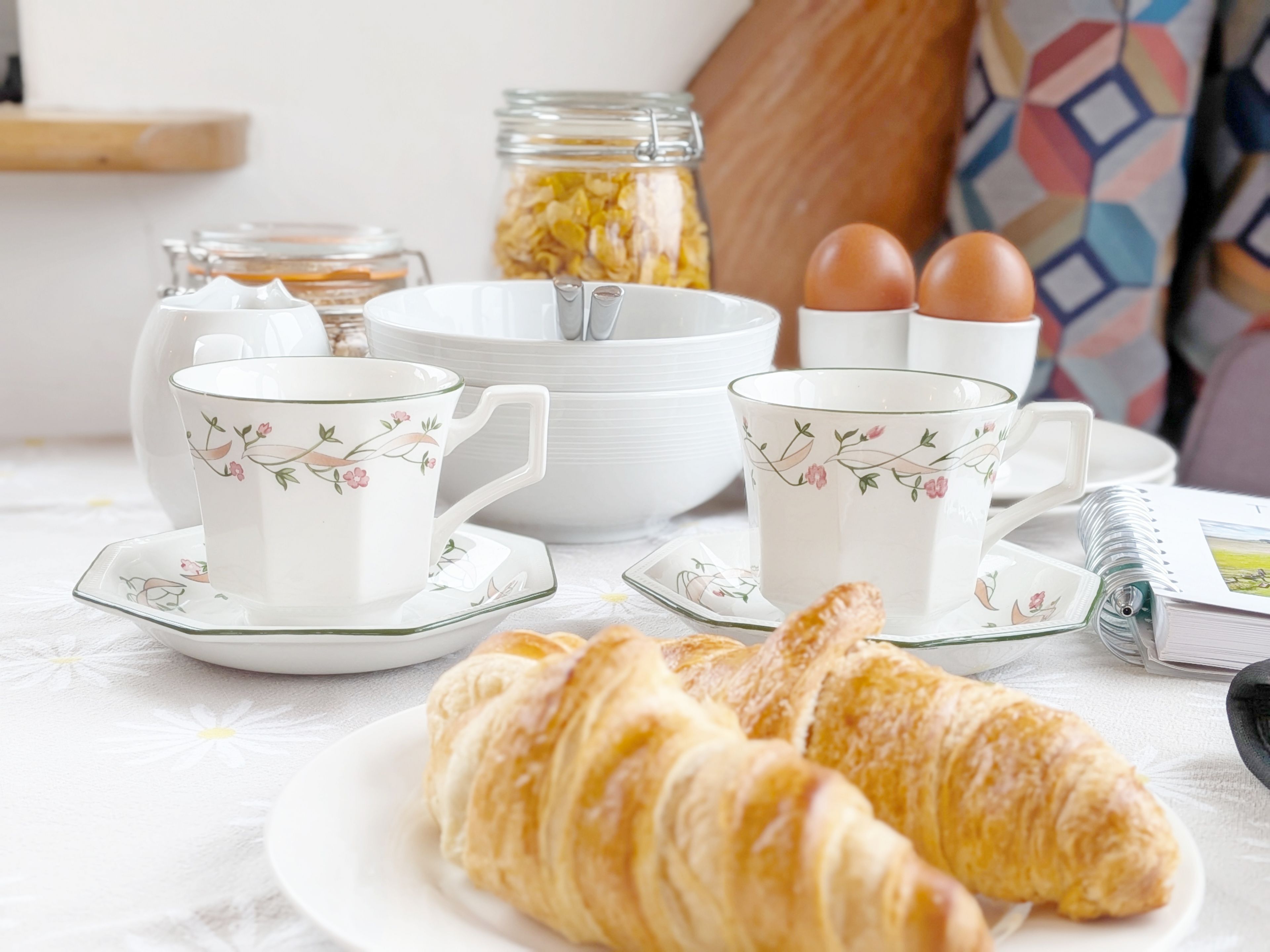 Une table mise pour le petit-déjeuner, avec des croissants, des tasses à thé et des œufs.