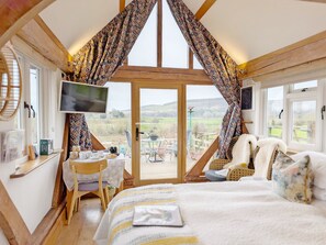 Une chambre confortable avec un grand lit, un téléviseur fixé au mur et une vue sur la campagne, visible à travers une porte vitrée.