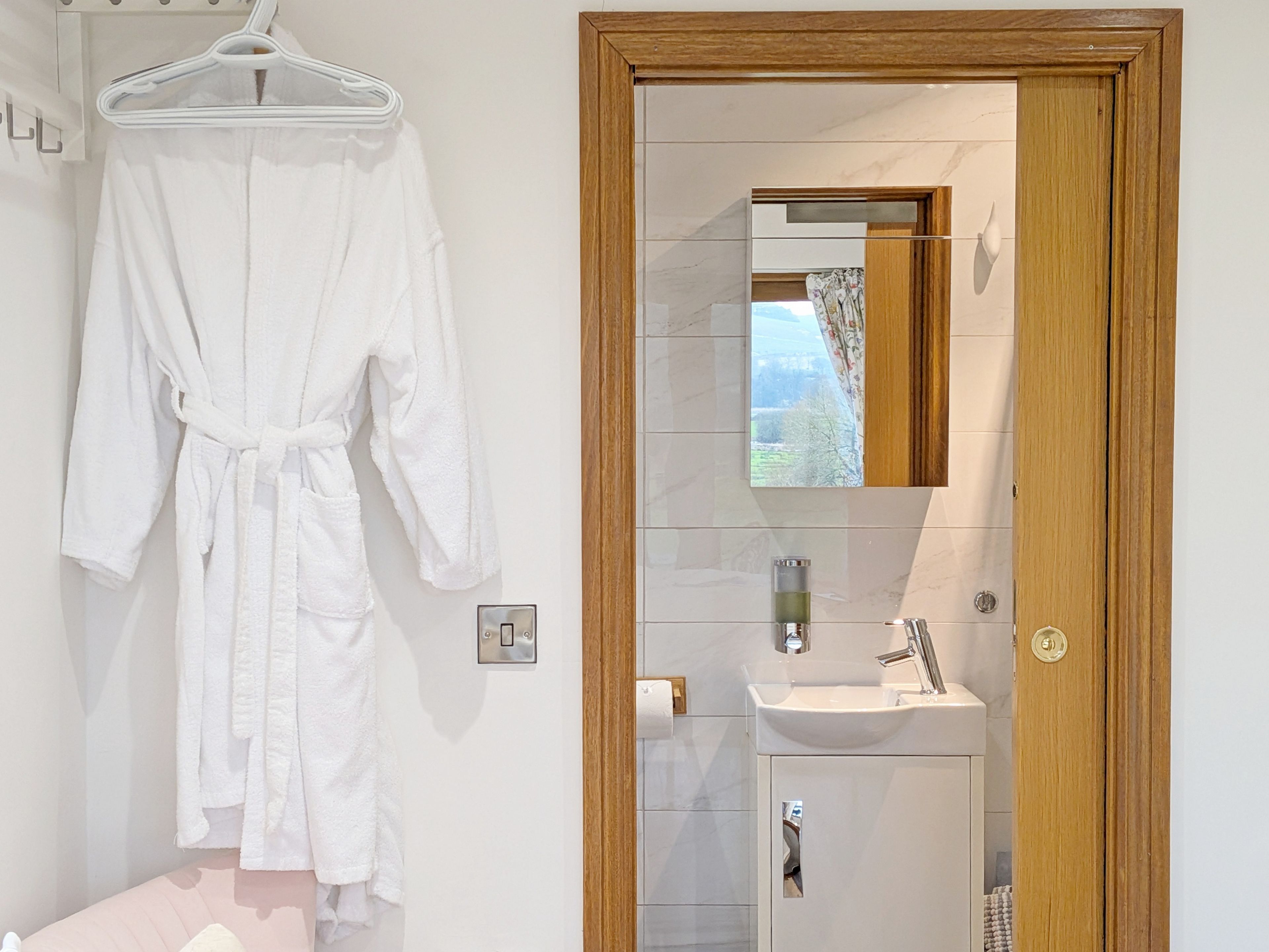 A bathroom with a wooden door, a mirror, a sink, and a towel rack with a white robe hanging.