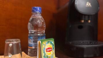 A wooden tray with a Lipton tea box, a water bottle, a coffee maker, and a glass on a table.