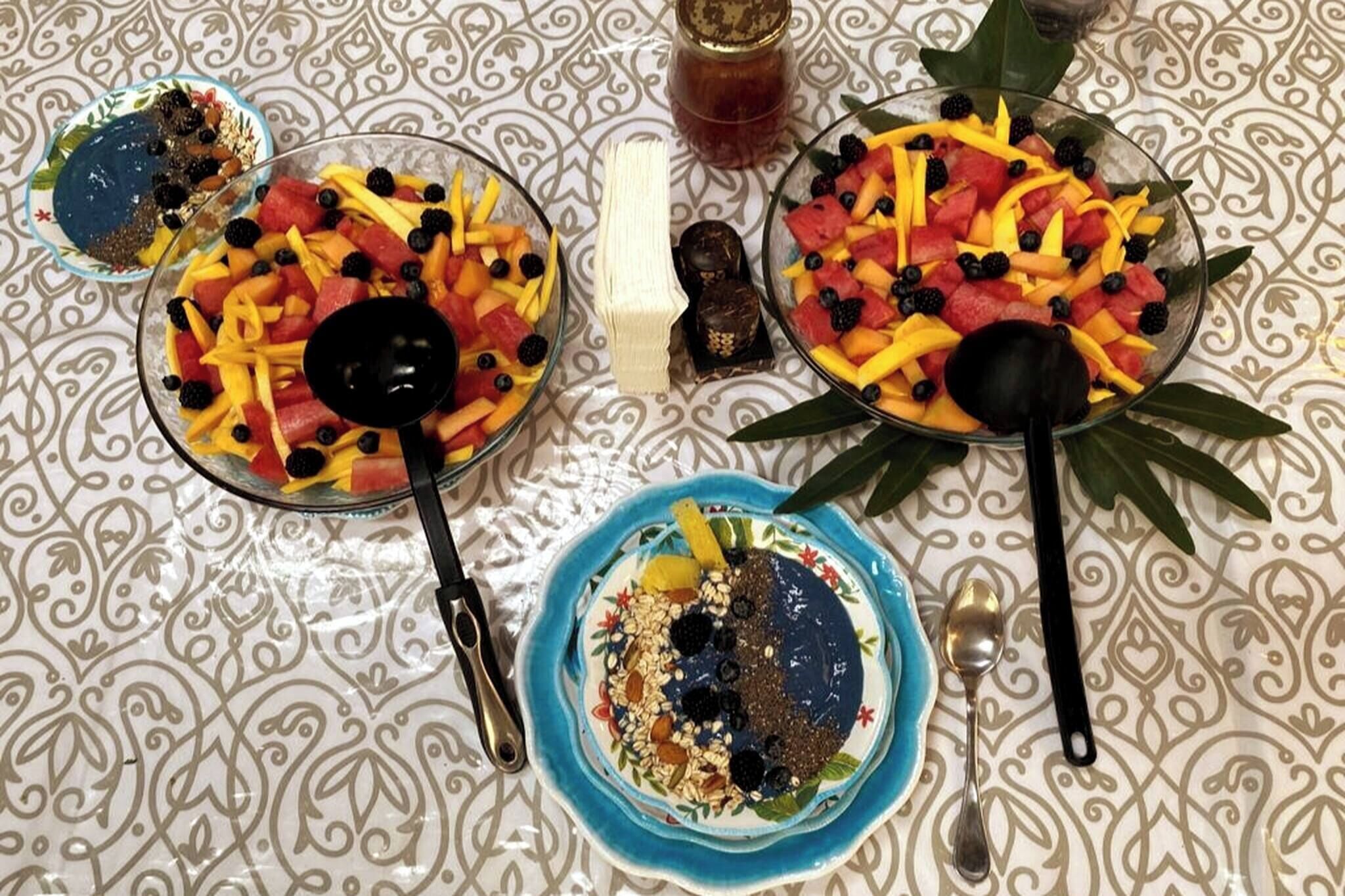 A table with three bowls of fruit salad and a small bowl of granola.