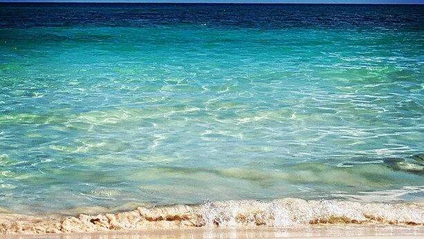 Ein Strand mit klarem türkisblauem Wasser und einem sandigen Ufer unter einem strahlend blauen Himmel mit weißen Wolken.
