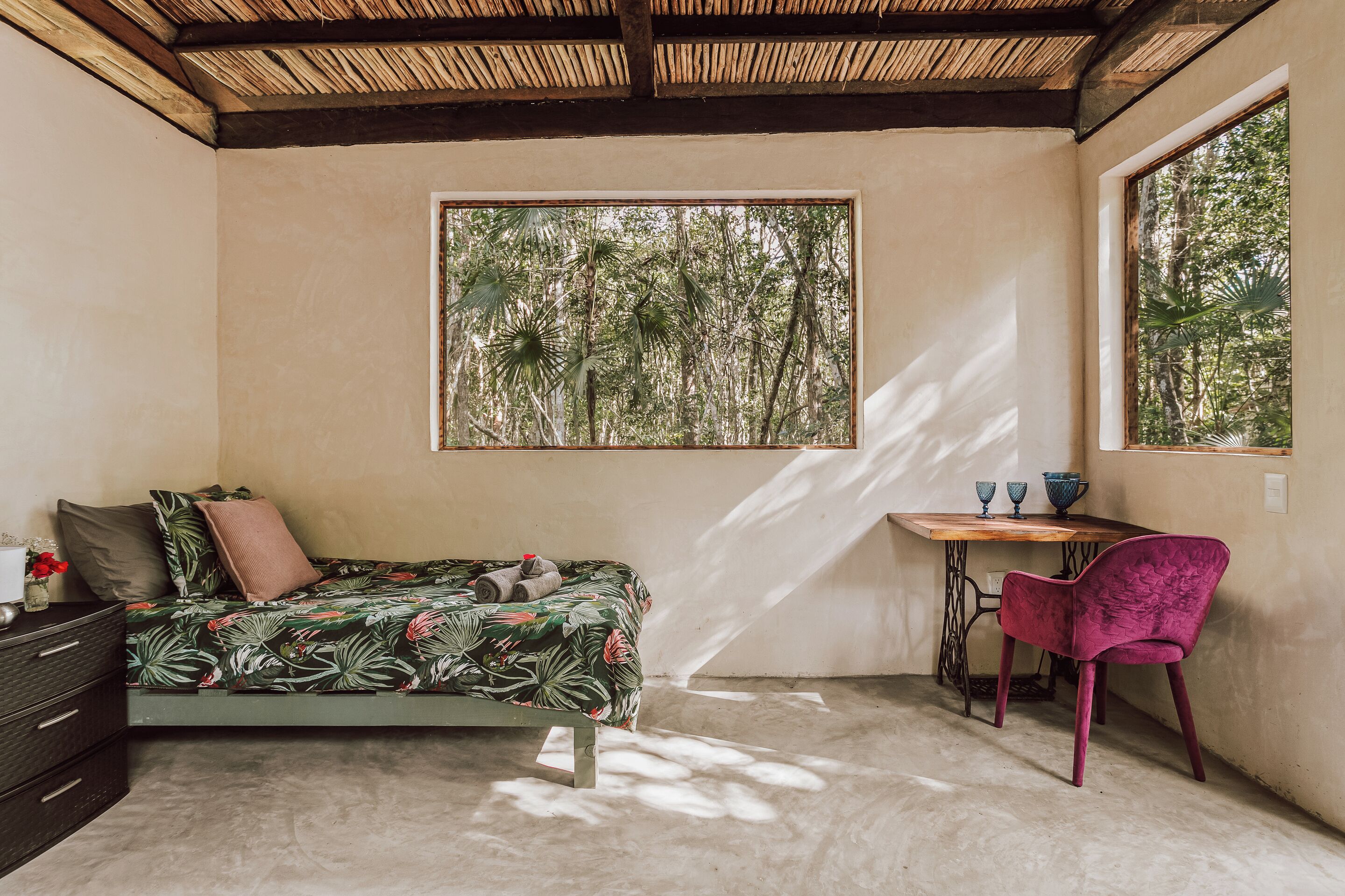 Un dormitorio con cama, escritorio, silla y ventana con vista a árboles.