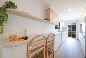 A modern kitchen with white cabinetry, a white countertop, and a built-in bench with woven seats. - Broadwater Breeze – Perfect Location, Ocean Breezes & Island Views (Airlie Beach)