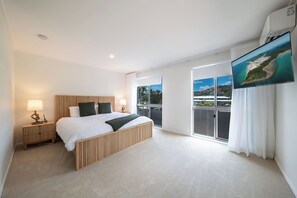 A modern bedroom with a large bed, a nightstand, a wall-mounted TV, and a balcony with a view. - Broadwater Breeze – Perfect Location, Ocean Breezes & Island Views (Airlie Beach)