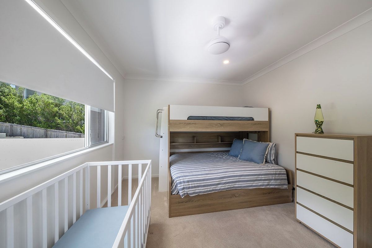 A bedroom with a bunk bed, a white dresser, and a window with a view of greenery.
