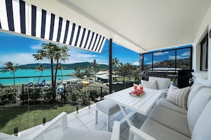 A balcony with a white table, white chairs, and a grill. - Broadwater Breeze (Airlie Beach)