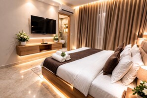Un dormitorio de hotel moderno con una cama grande, un televisor de pantalla plana, un mueble de madera y un baño visible a través de una puerta.