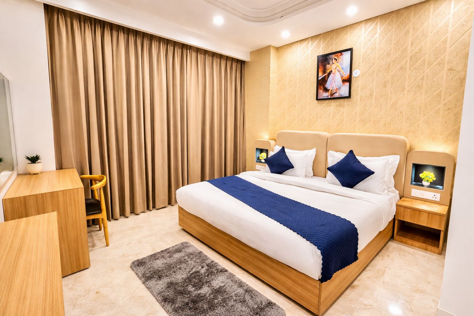 A modern hotel room with a large bed, a desk, a chair, a nightstand, and a wall-mounted TV.