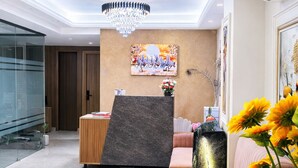 A modern lobby with a reception desk, a chandelier, a sofa, and a large window. - Dreamwood Hotel Near Sec 29 Gurgaon  (Gurugram)