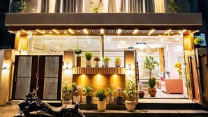 A multi-story building with air conditioning units, balconies, and a well-lit entrance with potted plants. - Dreamwood Hotel Near Sec 29 Gurgaon  (Gurugram)