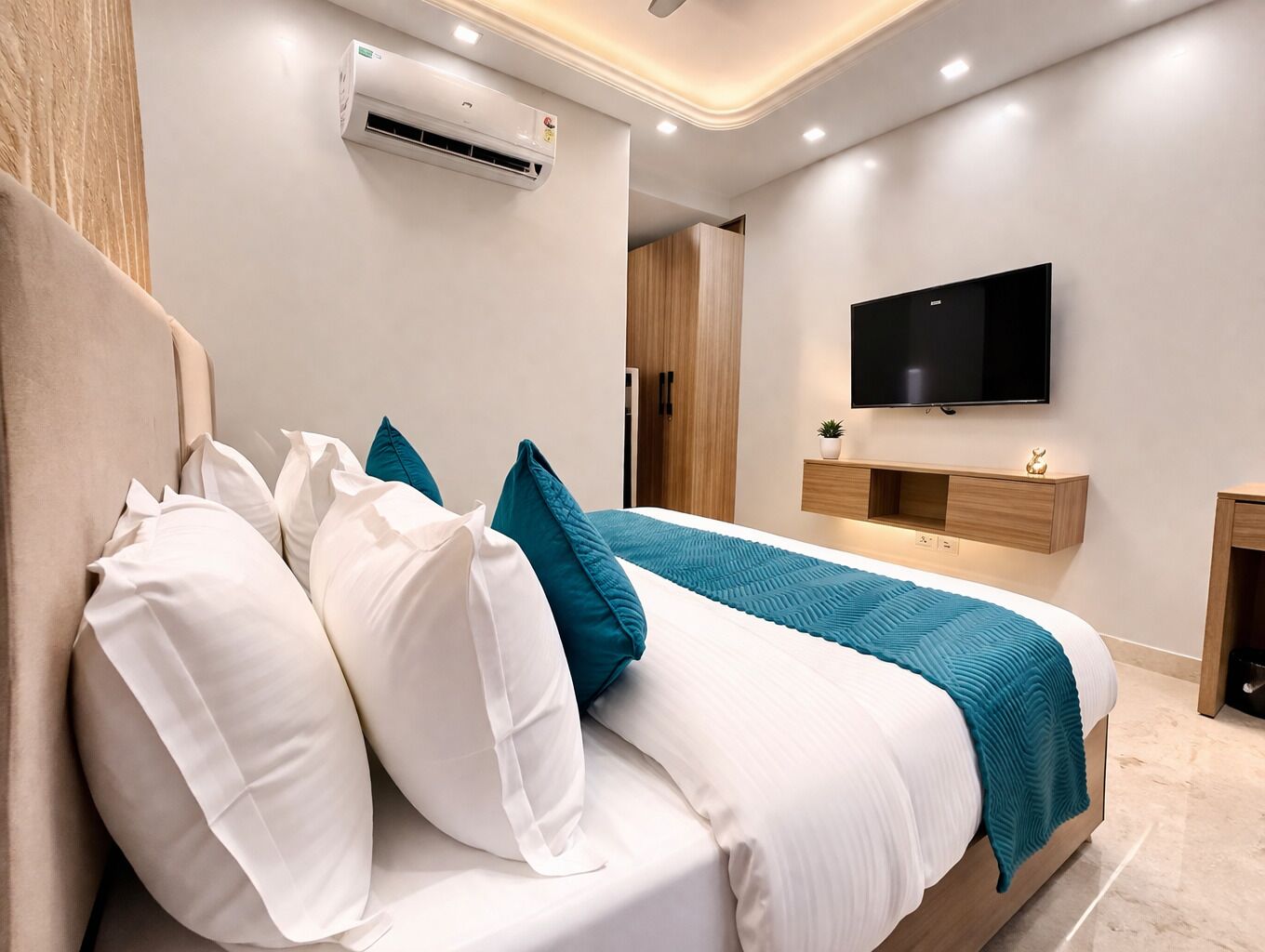 Un dormitorio moderno con una cama, almohadas blancas y turquesa, un televisor montado y un equipo de aire acondicionado.