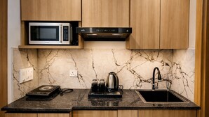 A kitchen with wooden cabinets, a microwave, a range hood, a sink, and a marble backsplash. - Dreamwood Hotel Near Sec 29 Gurgaon  (Gurugram)