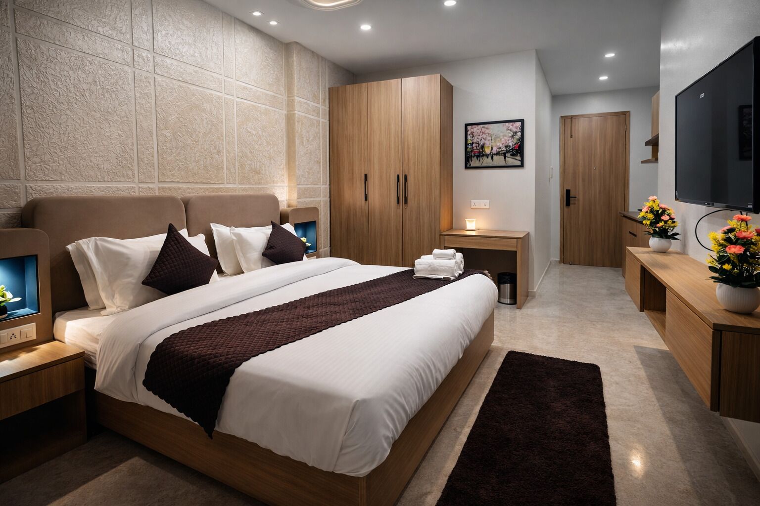 A modern hotel room with a large bed, wooden headboard, bedside tables, a TV, and a flat-screen TV mounted on the wall.