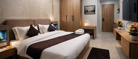 A modern hotel room with a large bed, wooden headboard, bedside tables, a TV, and a flat-screen TV mounted on the wall.