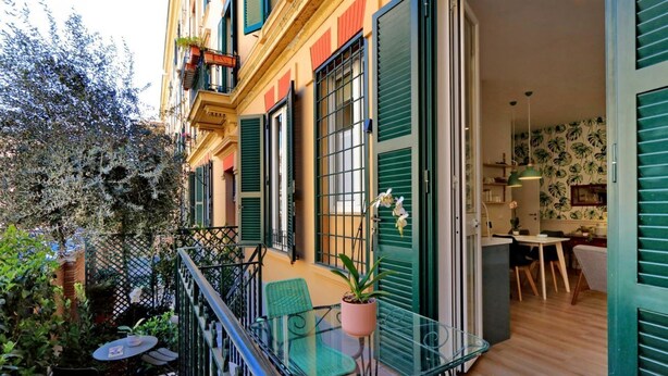 A balcony with a glass table and chairs, a potted plant, and a view of a dining area with a table and chairs. - Raffinato appartamento con piccolo giardino al Vaticano  (ROMA)
