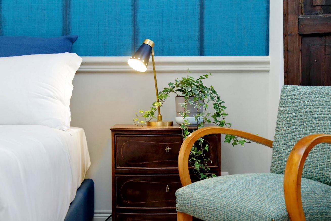 Une chambre à coucher bien rangée, avec un lit, une table de chevet dotée d’une lampe, une chaise et une plante en pot.