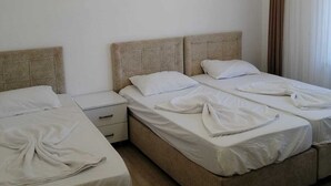 A hotel room with two beds, a bedside table, a wall-mounted air conditioner, and a ceiling light fixture. - İLKER APART OTEL (Silifke)