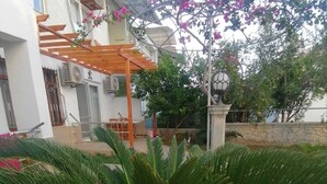 A residential area with a wooden pergola, a palm tree, and a statue. - İLKER APART OTEL (Silifke)