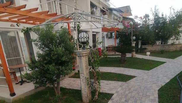 A courtyard with a paved walkway, a pergola, and a small tree. - İLKER APART OTEL (Silifke)