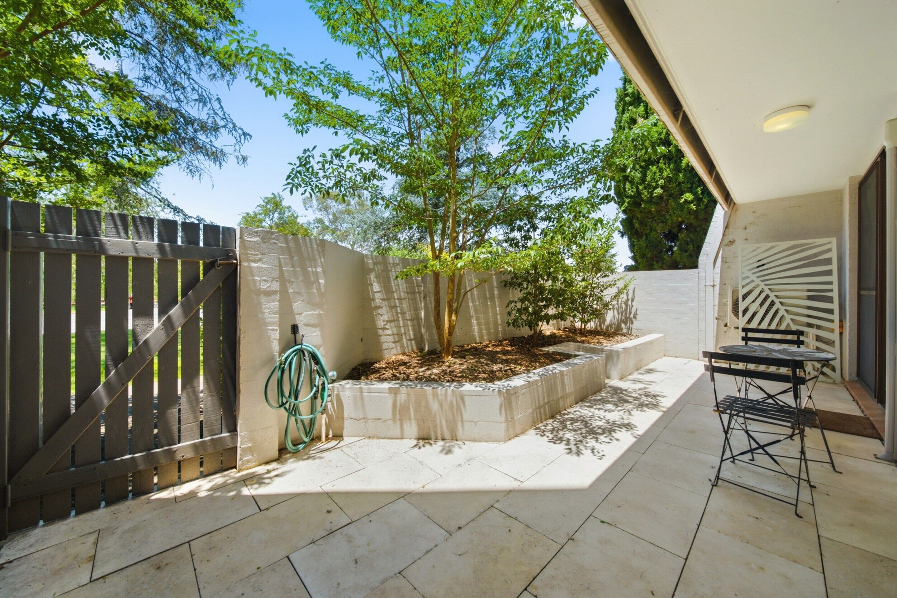 A patio area with a tiled floor, a wooden fence, a tree, and a metal table.
