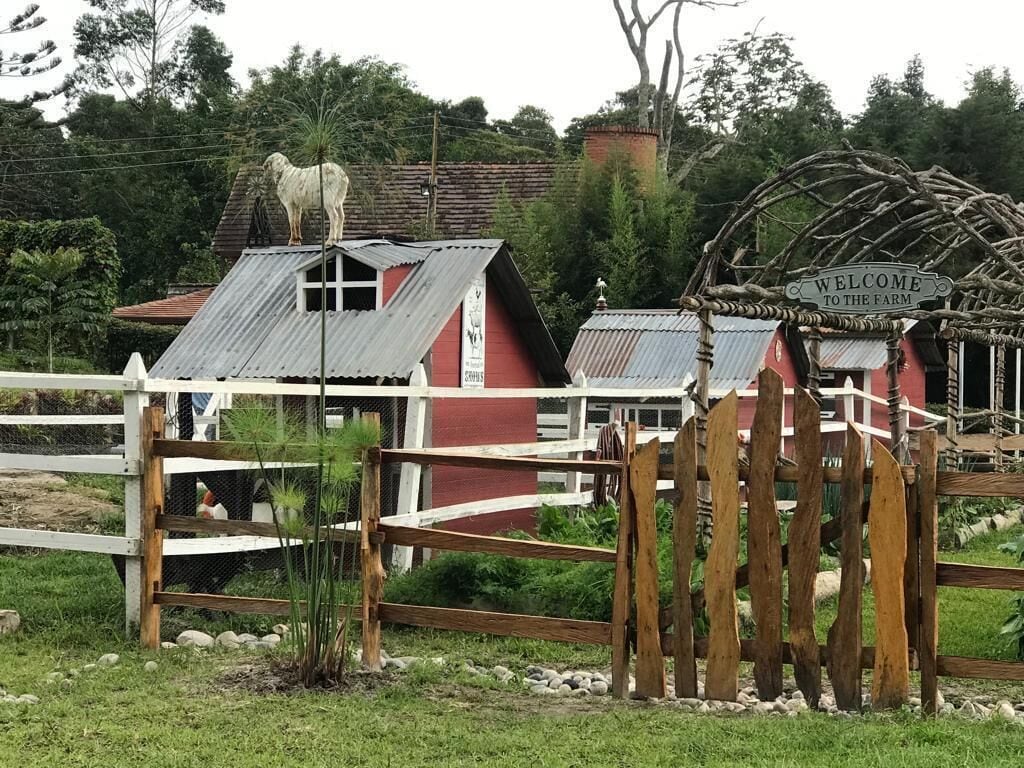 A rustic farm entrance with a wooden fence, a red barn, and a welcome sign.