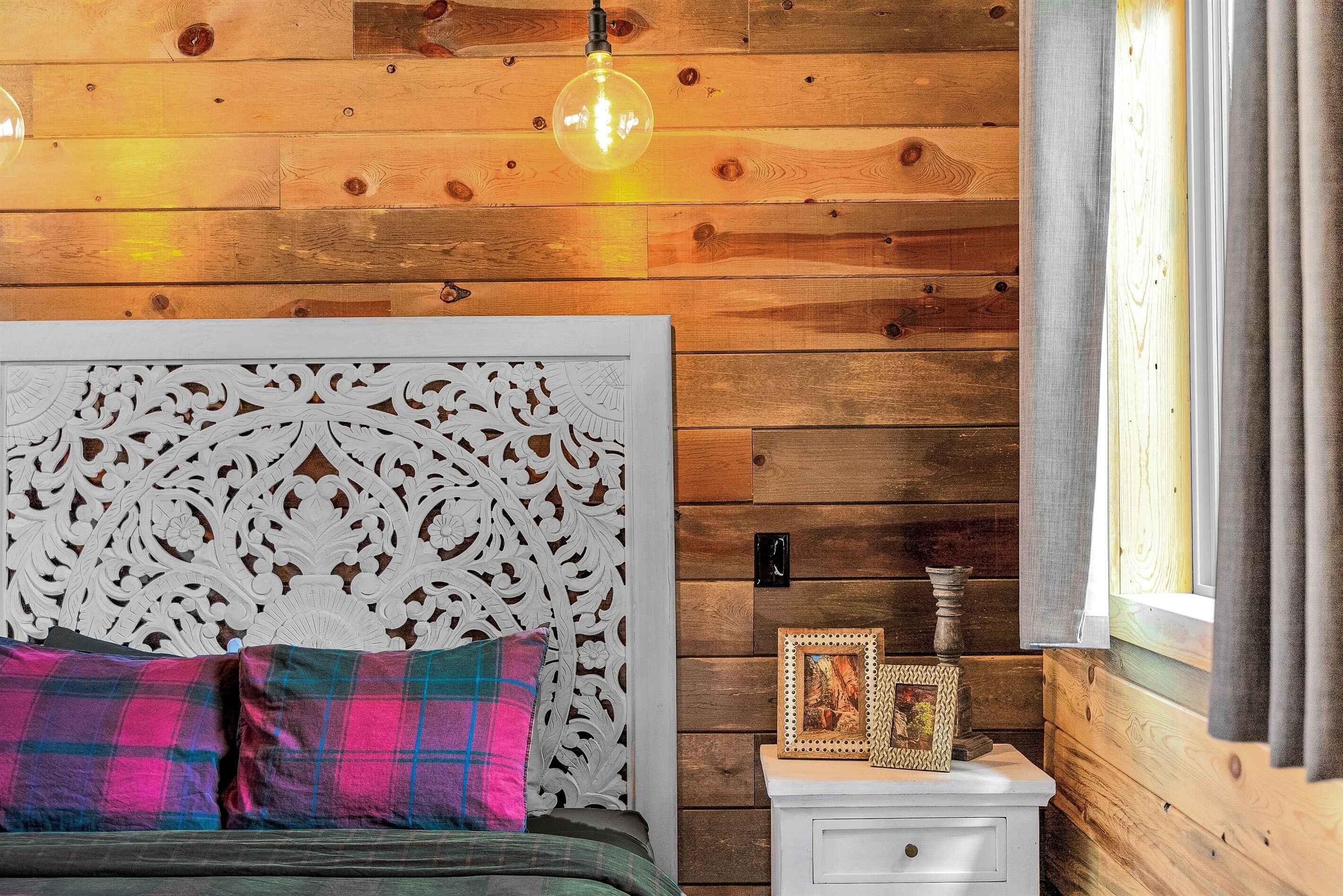 A wooden-paneled room with a bed, a white nightstand, and a hanging light fixture.