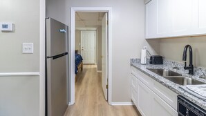 Eine kompakte Küche mit weißen Schränken, einem Edelstahlkühlschrank, einer Granitarbeitsplatte und einem schwarzen Wasserhahn.