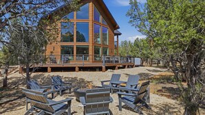 A multi-story wooden cabin with large windows, outdoor seating, and a deck. - Zion East Luxury | Private Hot Tub & Fire Pit (Orderville)