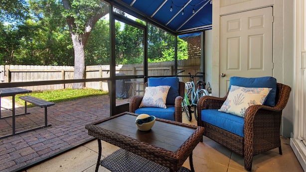 A covered patio area with wicker furniture, a table, and a bench.