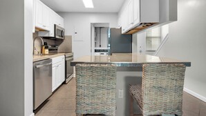 A modern kitchen with white cabinets, stainless steel appliances, and a central island with wicker chairs. - Hidden treasure minutes from Pensacola Beach with large pool area! (Gulf Breeze)