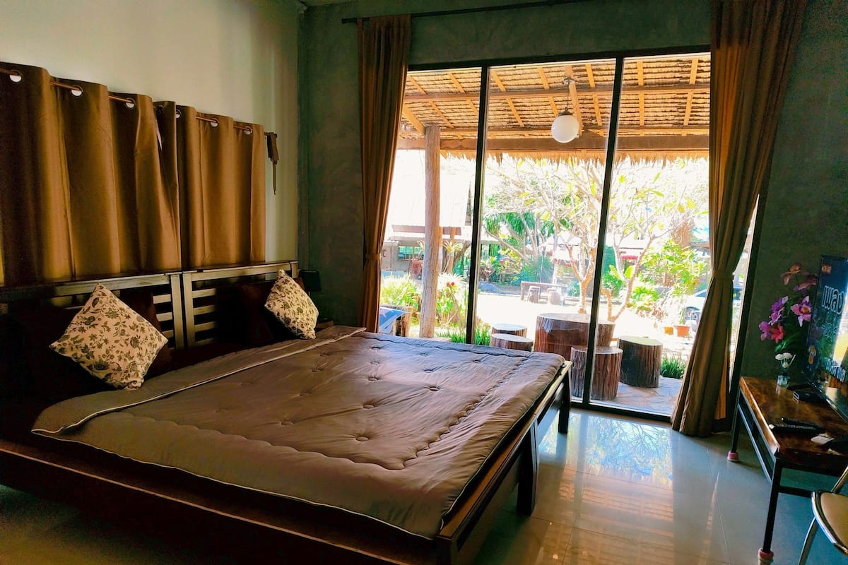 Une chambre avec un grand lit, une tête de lit en bois et une vue sur l’extérieur grâce à une porte-fenêtre coulissante.