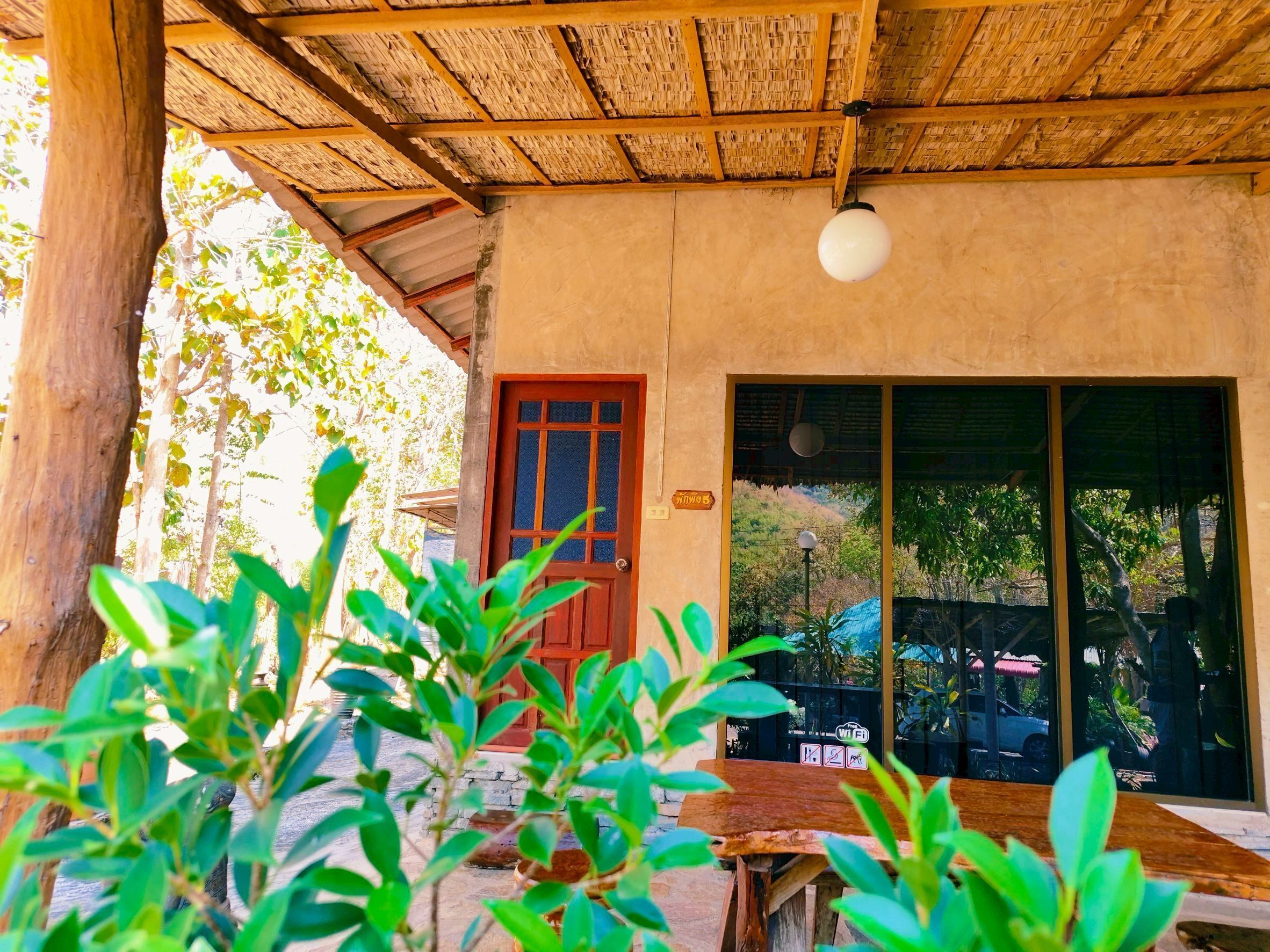 Un espacio al aire libre techado, con techo de madera, una puerta roja y un gran ventanal corredero que da a una vista del exterior.