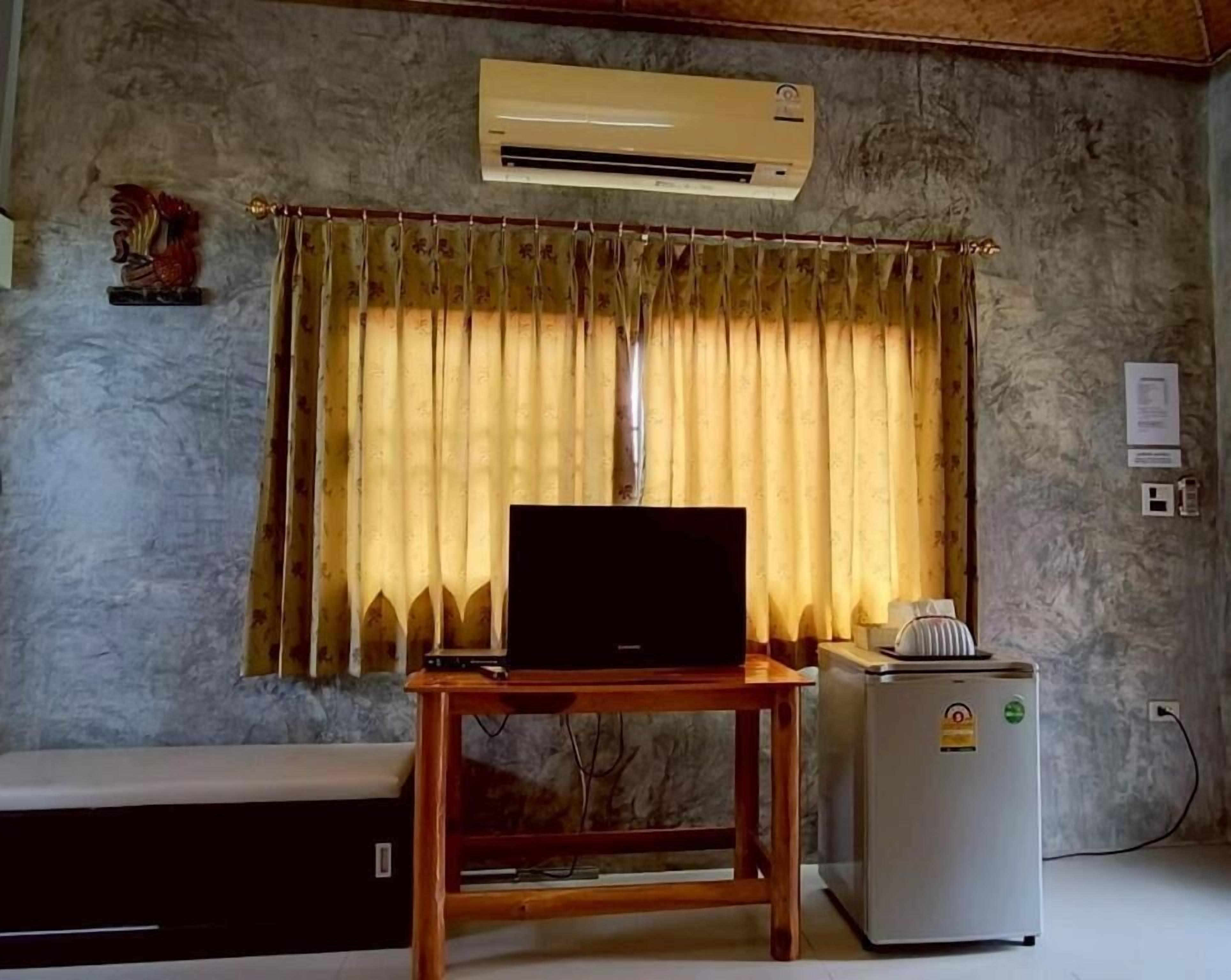 A room with a television on a wooden table, a small refrigerator, and a window with curtains.