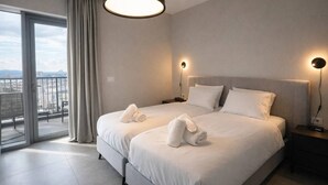 A modern hotel room with a large bed, two bedside tables, a balcony with curtains, and a city view. - 2 BR Apartment in Savyoney Tower (w/ safe room) (Jerusalem)