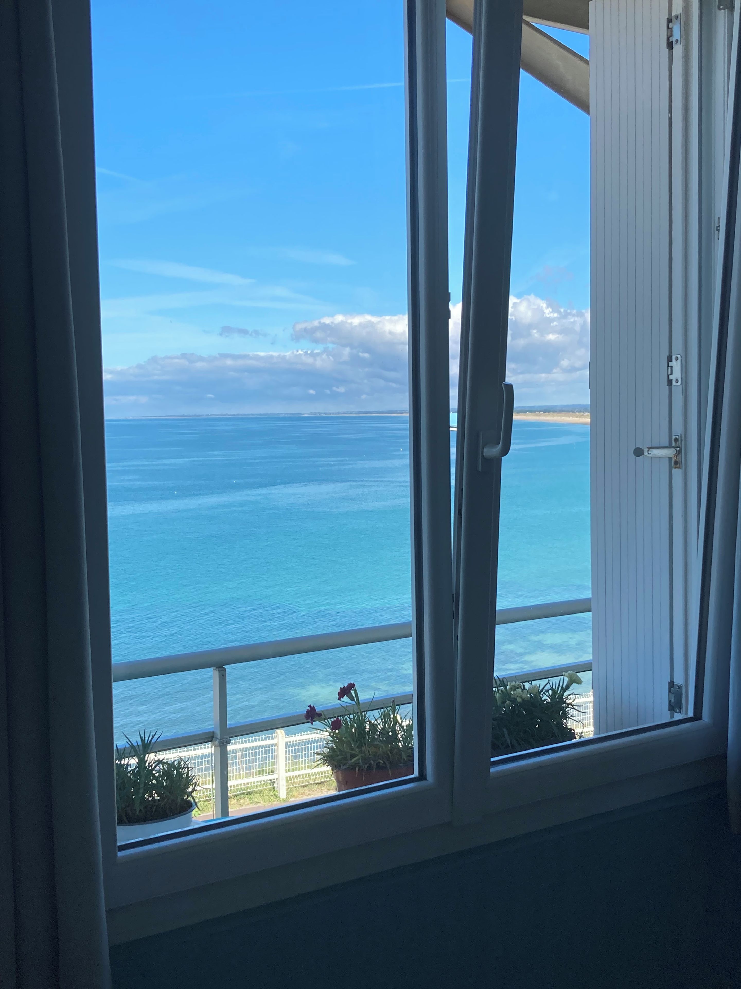 Quarto com vista para o oceano através de uma janela com porta branca e grade de metal.