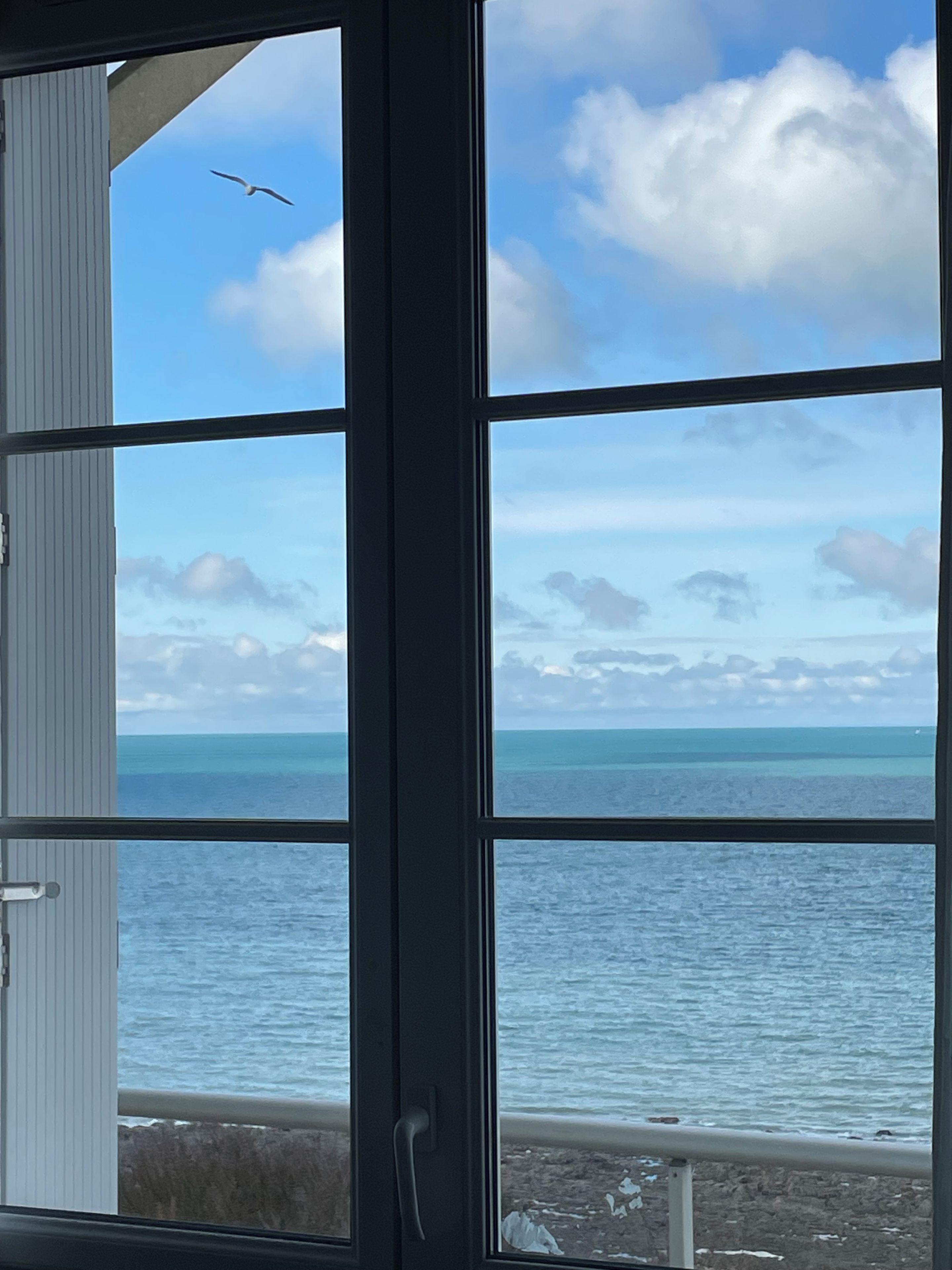 Uitzicht door een raam met een heldere lucht en de oceaan.