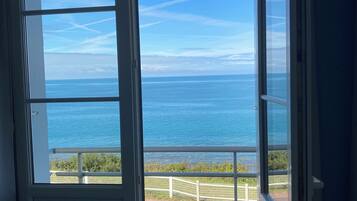 A view through a door to a balcony overlooking the sea with a clear sky.