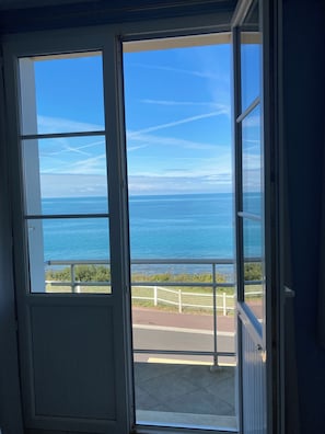 A view through a door to a balcony overlooking the sea with a clear sky. - Apartment with a view of the ocean (Donville-les-Bains)