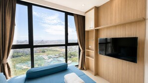 A modern hotel room with a large window, a flat-screen TV, a bed with blue bedding, and wooden paneling. - Room-sea View Room - Infinity Pool Near (Pattaya)