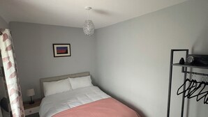 Une chambre à coucher comprenant un lit, une table de chevet, un luminaire suspendu, un tableau encadré au mur et une étagère noire sur laquelle sont posés divers objets.