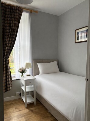 A bedroom with a single bed, a bedside table with a lamp, a framed picture on the wall, and a window with curtains. - Spacious Private Country House - king beds - extensive parking (Omagh)