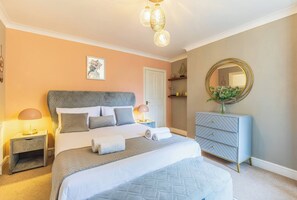 A bedroom with a large bed, bedside tables, a dresser, a mirror, and a hanging light fixture. - Spacious Seafront Apartment, Garden & Free Parking (Littlehampton)